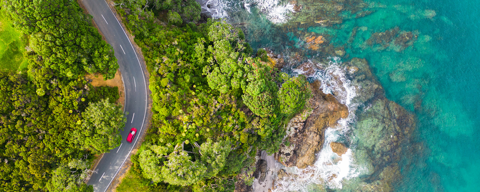 Drone photograph of a car driving on an ocean side road.